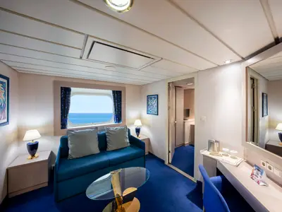 Blick in eine geräumige Premium Ocean View Aussenkabine an Bord der MSC Opera. Der Raum verfügt über ein blaues Sofa, einen Schreibtisch und ein Fenster mit direktem Blick auf das offene Meer.
