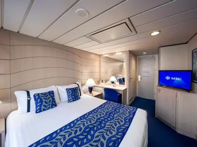 Balkonkabine der MSC Opera: Doppelbett mit blauen Kissen, Schminktisch, TV mit MSC Logo. Wellenförmige Holzwände prägen das helle Ambiente.