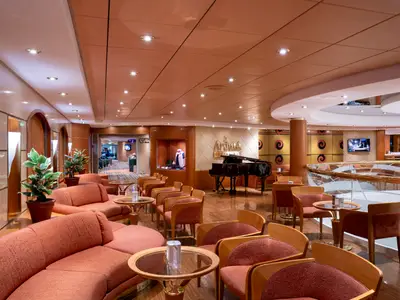 Einladende Aroma Coffee Bar an Bord der MSC Opera mit orangefarbenen Sitzgruppen, einem schwarzen Flügel und einer Bar im Hintergrund. Warme Beleuchtung schafft eine gemütliche Atmosphäre.