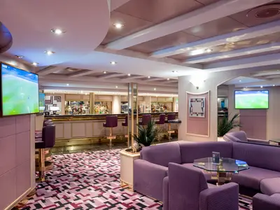 Bar-Lounge Sottovento Pub an Bord der MSC Opera. Lange Theke, violette Barhocker, lila Sofas und TVs mit Sportübertragung schaffen eine gemütliche Atmosphäre.