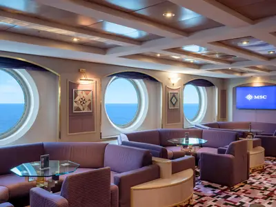 Innenausstattung des Sottovento Pubs auf der MSC Opera. Violette Sitzgruppen, Glastische und große runde Fenster mit Meerblick. Ein TV mit MSC Logo ist sichtbar.