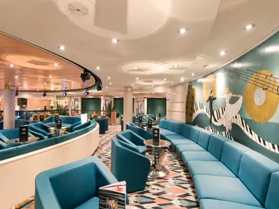 Die Cotton Club Bar-Lounge an Bord der MSC Opera. Türkisfarbene Sofas, Sessel und Tische auf buntem Teppich. Eine grosse Wandmalerei zeigt tanzende Figuren, Noten und Schallplatten an der Wand.