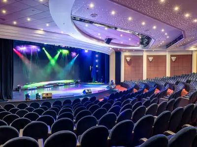 Weitwinkelaufnahme des Teatro dell'Opera an Bord der MSC Opera. Der große Saal mit blauen Samtsitzen blickt auf eine farbig beleuchtete Bühne. Die Decke funkelt mit sternenähnlichen Lichtern.