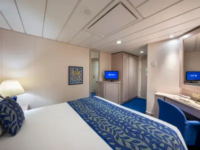 Geräumige Innenkabine der MSC Opera mit Doppelbett und blauer Bettwäsche. Ein TV, Schminktisch und blauer Teppich vervollständigen die funktionale Einrichtung.