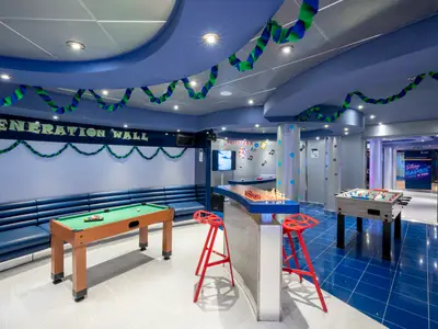 Ein bunter Teen Club an Bord der MSC Opera mit Billardtisch, blauem Sofa, Kicker, Schachbrett-Bar und TV. Helle, moderne Einrichtung in Blau- und Grüntönen.