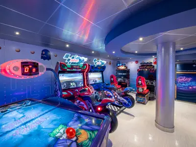Die lebhafte Spielhalle an Bord der MSC Opera zeigt Motorrad-Rennsimulatoren, Airhockey-Tisch und andere Automaten. Bunte Neonlichter und Pixel-Wandmotive prägen die Szenerie.