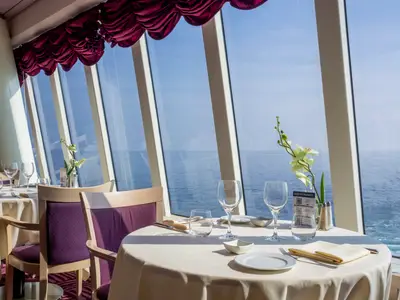 Restaurant an Bord der MSC Opera mit Panoramablick auf das Meer. Ein gedeckter Tisch mit Gläsern und Orchidee im Vordergrund.