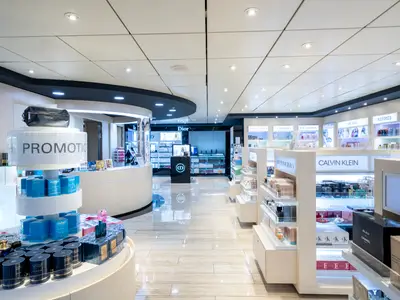 Ansicht der Parfümerie und Kosmetik-Boutique an Bord der MSC Opera. Verschiedene Markenprodukte auf hellen Regalen und Displays, darunter ein 'PROMOTION'-Display in der Mitte und Markennamen wie Dior, Lancôme und Calvin Klein an den Wänden. Der glänzende Boden reflektiert das Licht der Deckenstrahler. Es sind keine Personen zu sehen.