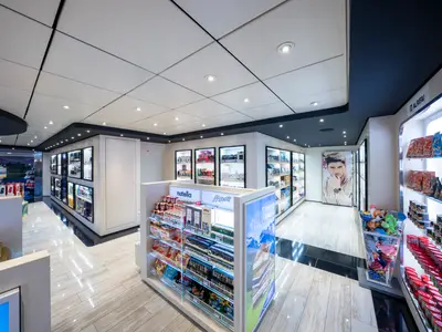 Ein moderner Duty-Free Shop an Bord der MSC Opera mit einer Vielfalt an Produkten. Regale bieten Süßigkeiten, Getränke, Parfüms und andere Artikel, hell erleuchtet von Deckenspots und Regalbeleuchtung.