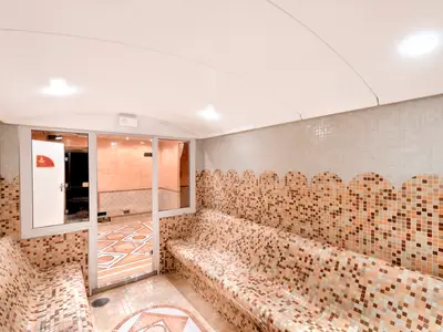 Ein geräumiges Dampfbad an Bord der MSC Opera mit Mosaikfliesen in Erdtönen, die Wände und geschwungene Bänke bedecken. Eine Glastür führt in einen angrenzenden Bereich.