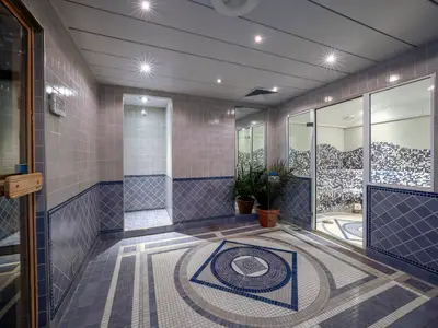 Spa-Bereich der MSC Opera. Ein Dampfbad mit blauen Mosaikfliesen, ein runder Fliesenboden in Blau und Grau, blaue Wände und Pflanzen. Helle Beleuchtung. Ohne Personen.