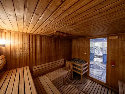 Helle Holzsauna an Bord der MSC Opera mit mehreren Bänken, Saunaofen und warmer Beleuchtung. Eine Tür führt zu einem gefliesten Wellnessbereich.
