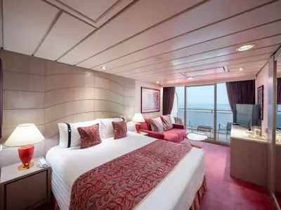 Eine geräumige Junior Suite Aurea an Bord der MSC Opera mit Doppelbett, rotem Sofa, modernem Dekor und einem Balkon mit Panoramablick auf das Meer bei Tageslicht.