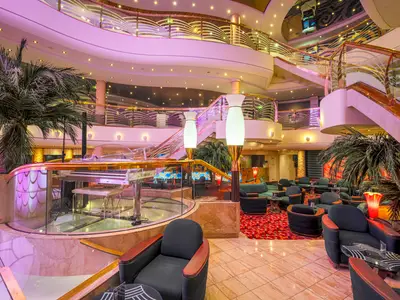 Atrium der MSC Orchestra: Runde Klavierbar, gemütliche Sitzgruppen, Palmen und eine geschwungene Treppe. Ambiente mit rosa Stimmungslicht.