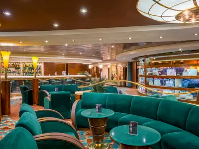 Elegante Bar-Lounge an Bord der MSC Orchestra mit Theke, reich gefuellten Regalen und gruenen Samtsofas. Rechts sind Produkte in einem angrenzenden Shop ausgestellt.