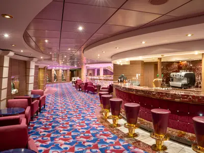 Die elegante Purple Bar der MSC Orchestra. Rote Marmortheke mit passenden Samthockern. Dahinter gemütliche rote Sessel und ein gemusteter Teppich in Rot und Blau.