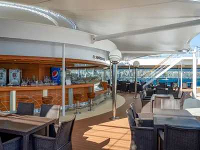 Die El Sombrero Bar an Bord der MSC Orchestra bei Tageslicht. Die überdachte Outdoor-Bar bietet Sitzbereiche und einen Tresen mit Meer- und Stadtblick.