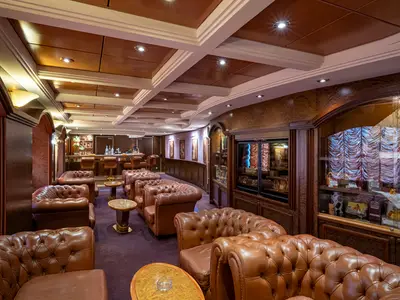 Elegante 'La Cubana' Lounge an Bord der MSC Orchestra mit braunen Ledersofas, Tischen, Bar und Vitrinen mit Auslagen.