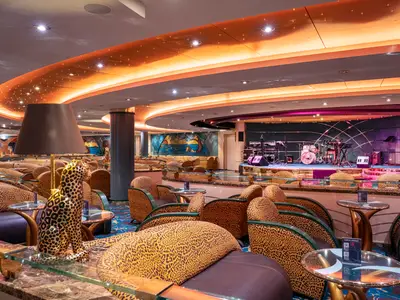 Blick in die The Savannah Bar an Bord der MSC Orchestra mit Bühne und Schlagzeug. Zahlreiche Tische und Sessel mit Leopardenmuster, sowie eine grosse Lampe in Form eines sitzenden Leoparden sind zu sehen.