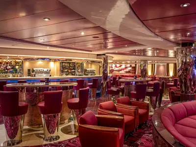 Elegante Shaker Lounge Bar der MSC Orchestra. Rote Samt-Barhocker, Sessel und Sofas um eine halbrunde Bar mit Getränken.