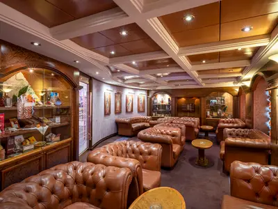 Elegante Cigarren-Lounge "La Cubana" an Bord der MSC Orchestra. Viele braune Ledersofas, kleine Tische und beleuchtete Vitrinen mit Spirituosen und Zigarren füllen den Raum.