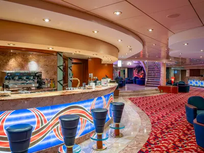 Die elegante L'Incontro Bar an Bord der MSC Orchestra. Eine lange Marmortheke mit leuchtender Front und Barhockern. Dahinter Sitzbereiche, Treppe und Rezeption.