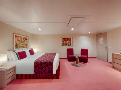 Geräumige barrierefreie Kabine an Bord der MSC Orchestra mit Doppelbett, roten Kissen, Nachttischen und einer Sitzecke. Roter Teppich und bunte Bilder.