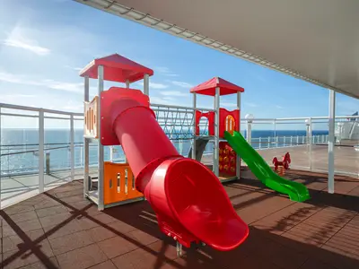 Spielplatz an Deck der MSC Orchestra mit bunten Rutschen, Kletterturm und Federwippe. Im Hintergrund das weite blaue Meer und Himmel.