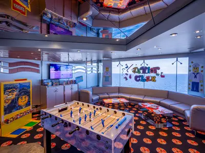 Der Junior Club an Bord der MSC Orchestra: Ein farbenfroher Raum mit Tischkicker, Mosaik-Bausatz, TV und bequemer Sitzgruppe. Große Fenster bieten einen weiten Blick auf das offene Meer.