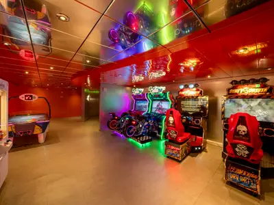 Arcade-Spielehalle an Bord der MSC Orchestra mit Rennsimulatoren, Airhockey und Greifautomat. Bunte Neonlichter der Automaten spiegeln sich an der Decke. Rote Wände. Ein lebhafter Unterhaltungsbereich.