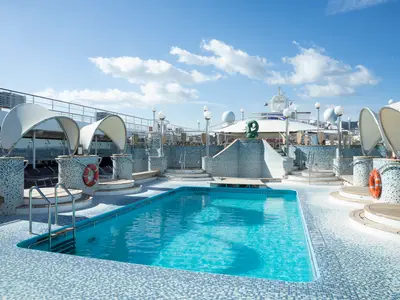 Sonniges Pooldeck an Bord der MSC Orchestra mit einem leuchtend blauen Swimmingpool und mehreren Whirlpools. Die Becken sind mit Mosaikfliesen verziert, weiße Sonnensegel spenden Schatten.
