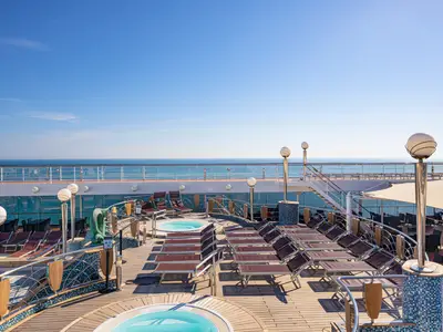 Ein sonniges Sonnendeck an Bord der MSC Orchestra mit einem Whirlpool, Reihen von Liegestühlen, und einem weiten Blick auf das offene Meer und blauen Himmel. Eine Treppe führt zu einer unteren Ebene.