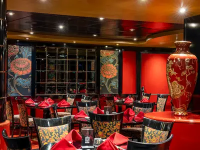 Elegantes asiatisch inspiriertes Spezialitätenrestaurant 'Shanghai' an Bord der MSC Orchestra. Rote Akzente, gemusterte Stühle, Tische mit roten Servietten und eine große rote Drachen-Vase prägen den Raum.