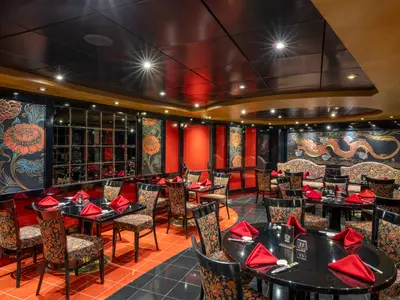 Restaurant Shanghai an Bord der MSC Orchestra. Elegante Einrichtung mit schwarzen Tischen, roten Servietten und gemusterten Stühlen. Wände mit goldenen Blumen- und Drachenmotiven.