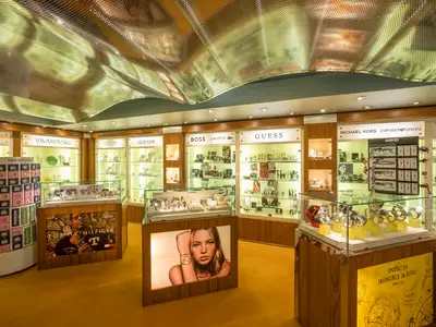 Ein heller Uhren- und Schmuckladen an Bord der MSC Orchestra mit Auslagen der Marken Swarovski, Tommy Hilfiger, Calvin Klein und Guess. Elegantes Design mit Goldtönen und geschwungener Decke.