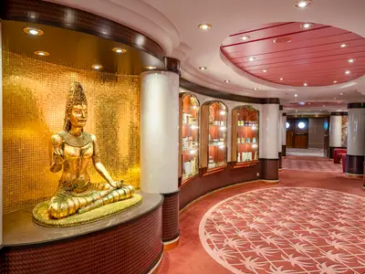 Der elegante Spa-Bereich an Bord der MSC Orchestra. Eine goldene, sitzende Statue vor einer Mosaikwand. Geschwungene Gänge mit roten Teppichen und beleuchteten Vitrinen.
