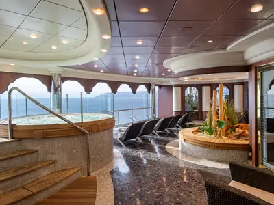 Geräumiger Spa-Thermalbereich an Bord der MSC Orchestra mit einem sprudelnden Whirlpool, mehreren Rattan-Liegestühlen und einer dekorativen Pflanzeninsel. Große Fenster bieten einen weiten Blick auf das offene Meer.