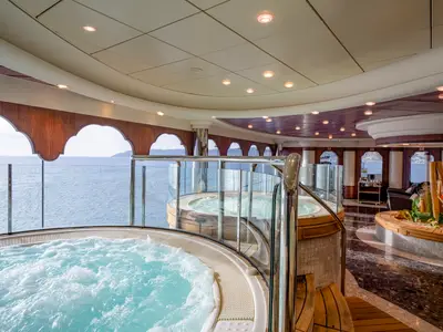 Luxuriöser Spa-Bereich an Bord der MSC Orchestra mit sprudelnden Whirlpools und Meerblick. Elegantes Design mit Holz und Glas, stimmungsvoll beleuchtet für Entspannung.