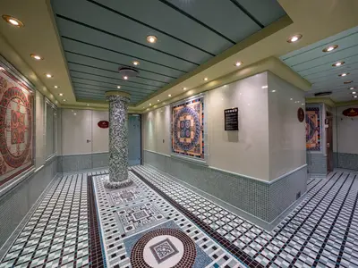 Thermalbereich des MSC Aurea Spa an Bord der MSC Orchestra. Helle Wände, farbenfrohe Mosaikfliesen auf Boden und Wänden. Zugänge zu Sauna und Dampfbad sind zu erkennen. Die Decke hat eingelassene Lichter.