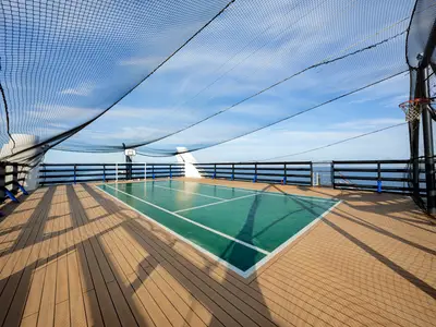 Ein sportlicher Mehrzweckplatz auf dem Sonnendeck der MSC Orchestra, umgeben von einem Schutznetz, mit einem Basketballkorb und Blick auf das weite Meer.