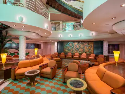 Elegante Lounge an Bord der MSC Poesia. Orangefarbene Sofas, Sessel, gemusterter Teppich. Geschwungene Decke mit Lichtern, große Kunstwand, Pflanzen, Stehlampen.