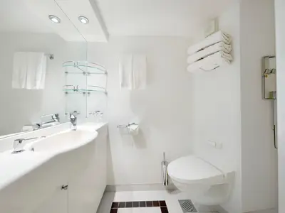 Ein helles Badezimmer an Bord der MSC Poesia mit Waschbecken, Spender, Spiegel, Toilettenpapier und Toilette. Die Einrichtung ist modern und minimalistisch gehalten.