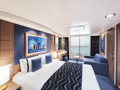 Helle Balkonkabine der MSC Poesia mit Doppelbett, blauem Sofa und Meerblick vom Balkon. Moderne Einrichtung mit blauen Wänden, Holzelementen und Kunstwerk.