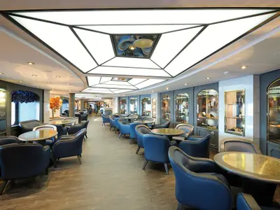Die elegante Bar-Lounge 'Il Grappolo d'Oro' an Bord der MSC Poesia mit Reihen blauer Sessel und runden Tischen. Mehrere Vitrinen mit Wein und Delikatessen säumen die Wände, eine moderne Deckenbeleuchtung erhellt den Raum.
