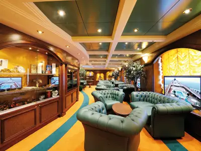Luxuriöse Lounge der MSC Poesia mit grünen Chesterfield-Sesseln, dunklen Holzeinbauten und beleuchteten Vitrinen. Grüne Kassettendecke und warme Beleuchtung.