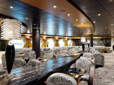 Luxuriöse Zebra Bar an Bord der MSC Poesia. Mit schwarz-weiß gemusterten Sesseln, dunklen Marmortischen und goldenen Akzenten. Designer-Lampen erhellen den eleganten Raum.