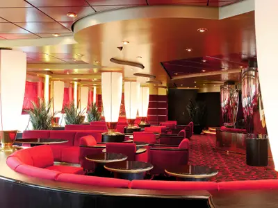 Die stilvolle Pigalle Lounge an Bord der MSC Poesia. Rote Samtsofas, runde Tische, hohe beleuchtete Säulen und eine goldfarbene Decke schaffen ein elegantes Ambiente. Ohne Personen.