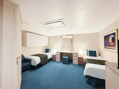 Barrierefreie Innenkabine an Bord der MSC Poesia mit zwei Einzelbetten, blauem Sessel und Schminktisch. Helle Wände, blauer Teppich. Über dem linken Bett ein Klappbett.