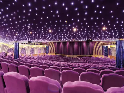 Theatersaal Teatro Carlo Felice an Bord der MSC Poesia. Zahlreiche lila Samtsitze und eine breite Bühne mit dunklen Vorhängen. Die dunkle Decke ist kunstvoll mit vielen sternförmigen Lichtern beleuchtet.