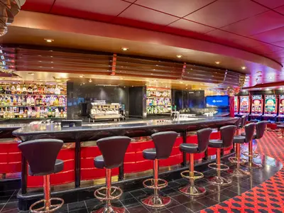 Blick auf die leere, rote und schwarze Bar im Casino Royal an Bord der MSC Poesia, umgeben von Slot-Maschinen und Lichtern.
